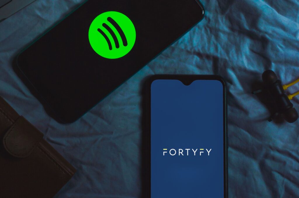 Smartphone showing the FORTYFY logo next to a phone with Spotify: how to switch music distributors without losing streams